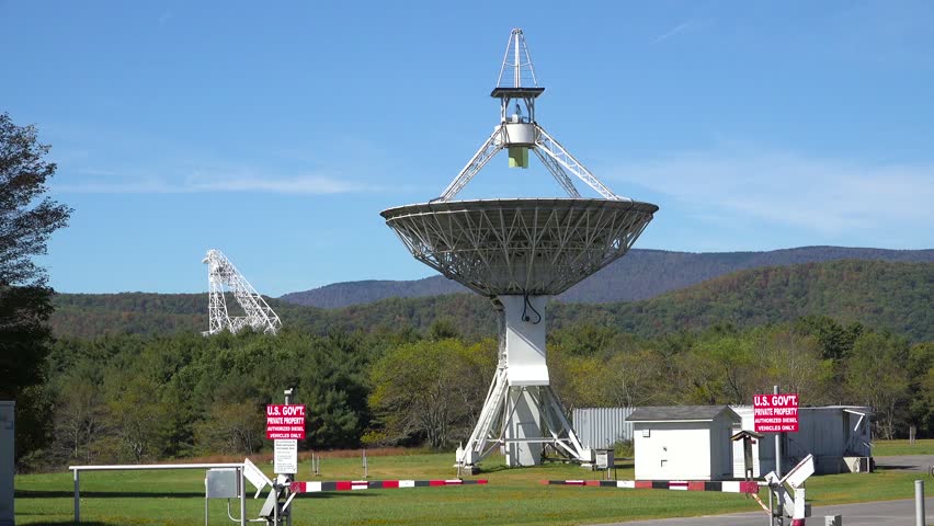 Footage showcases large radio telescopes on sunny day. This motion clip captures vast forest landscape with mountains, under clear blue sky, highlighting scientific research facility
