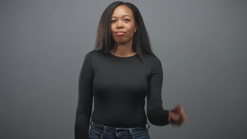 Young woman touches temple with index finger in studio, wearing black shirt and jeans, neutral smile and direct gaze; thoughtful insight idea.