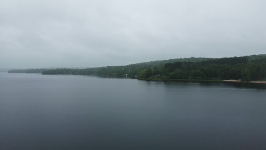 Misty shoreline and calm waters under overcast skies, drone pullback, empty backdrop