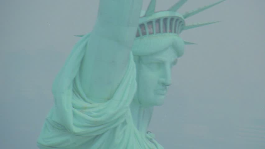 Cinematic aerial footage showing detailed view of copper statue face. Statue of Liberty monument shrouded in fog. Iconic New York City landmark with atmospheric lighting and subtle motion.