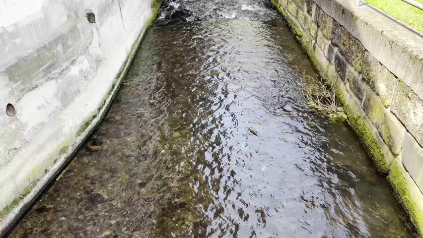 An artificial canal flows right past a house; it passes under a bridge. Above it stands an old wooden building., tilt up shot