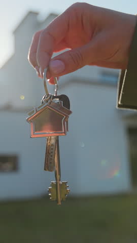 Vertical video Close-up of house key in the hand of woman house against the background. Real estate concept for buying a new home.