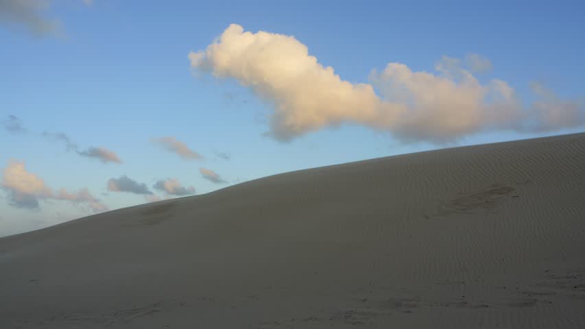 Beautiful sand dune contrasting with a clear blue sky as soft white clouds float by