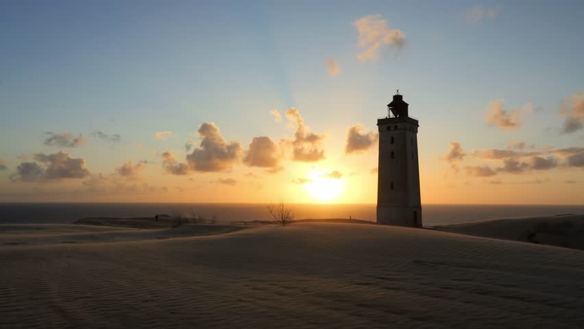 Time-lapse of the setting sun disappearing over the horizon behind the iconic Rubjerg Knude Lighthouse in Denmark