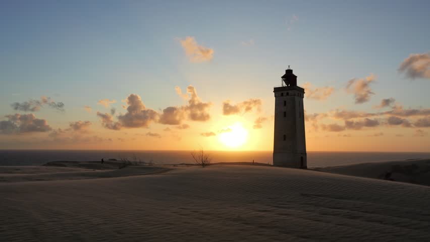 Golden sun setting over the North Sea behind the iconic Rubjerg Knude Lighthouse in Denmark