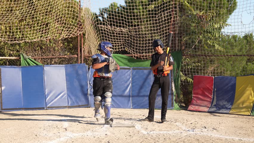 Slow motion view of a kid batter swinging and hitting the ball during a youth league game while the catcher is waiting behind him