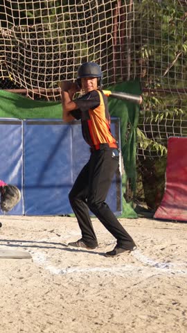 Teen boy in uniform swinging a baseball bat during training. Slow motion footage of a young athlete hitting the ball in a batting cage