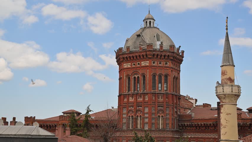 Historic Phanar Greek Orthodox College, known as the Red Castle, standing next to a mosque minaret against a blue sky with clouds in Istanbul