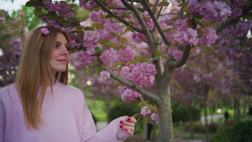 Woman enjoys cherry blossoms in a park during springtime while standing under a blooming tree with pink flowers