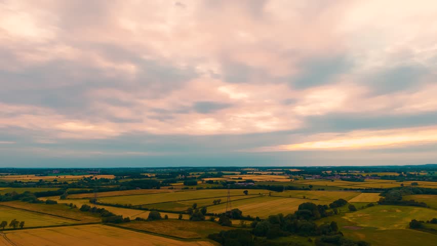 Timelapse patchwork farmland beneath colorful sunset cloudscape. Panoramic agricultural landscape with golden grain fields forest belts distant villages and rural horizon. Evening sky with moving