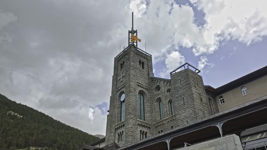 Majestic stone bell tower of the Sanctuary of Nuria, located in the Pyrenees of Catalonia, with the Catalan flag waving against a dramatic sky full of fast moving clouds