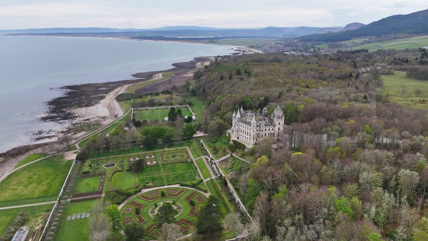 A drone shot of Dunrobin Castle facing towards the sea, with dense trees on both sides, in Scotland