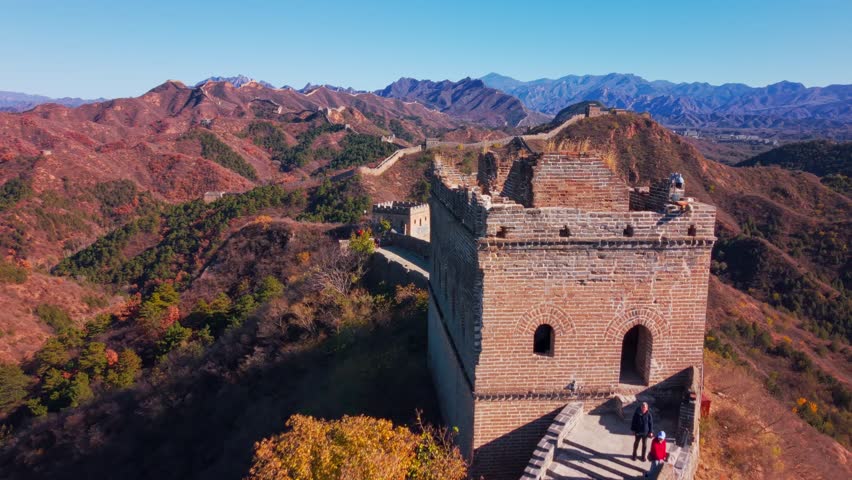 High angle view of the historic Great Wall of China winding across autumn hills with stone watchtowers under a clear blue sky