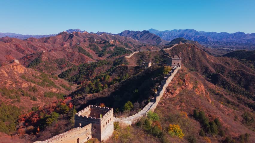 High angle view of the historic Great Wall of China winding across autumn hills with stone watchtowers under a clear blue sky