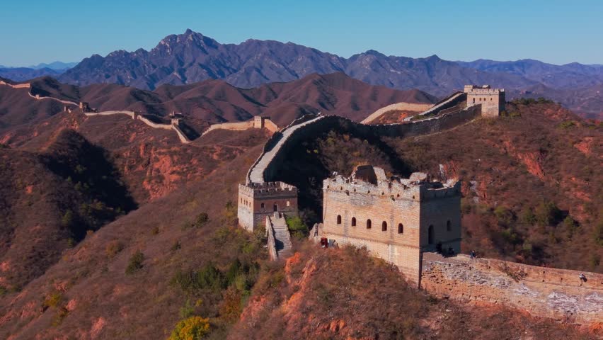 Scenic high angle view of the historic Great Wall of China winding through autumn mountains and hills with a traditional stone watchtower under a clear blue sky