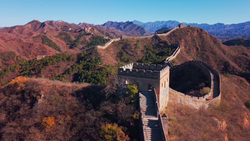 High angle view of the historic Great Wall of China winding across autumn hills with stone watchtowers under a clear blue sky