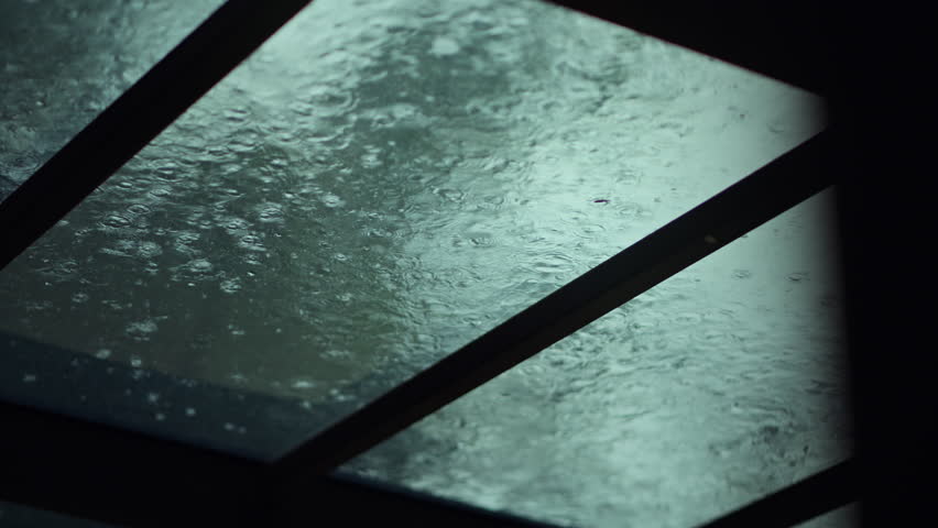 Close up of raindrops falling on transparent glass roof during heavy rain, abstract wet raindrop ripples on glass window background for monsoon season, stormy weather, cozy stay home, and peaceful nature concept.