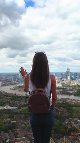 Rear view of a tourist woman looking at the panoramic view of the skyline of London, England, during a sunny summer day