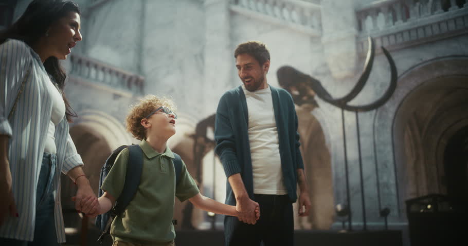 Natural History Museum Trip: Father Watches and Smiles as Mother and Young Son Explore Towering Mammoth Tusks, Family Learning About Ancient Creatures and Enjoying Fun Time Together.