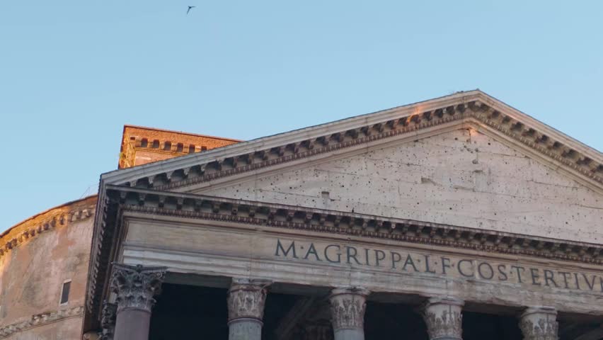 Low angle architectural view of the Pantheon in Rome featuring massive Corinthian columns and detailed ancient Roman stonework against a clear blue sky in Italy.