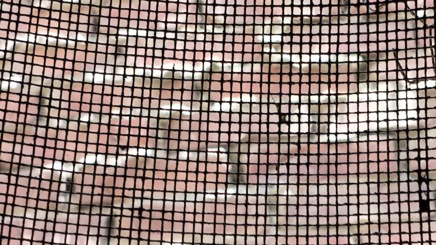 Close up of a window wire mesh screen with blurred red brick wall background