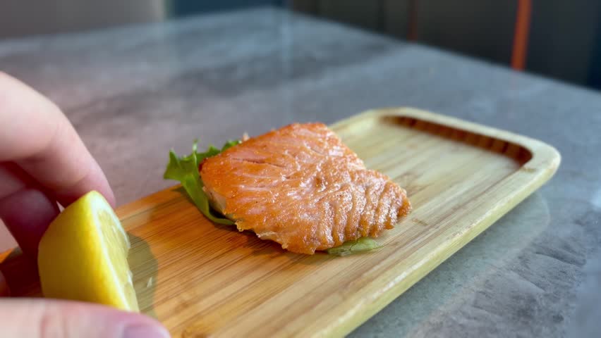 Sprinkling lemon juice on a portion of grilled salmon served at a restaurant