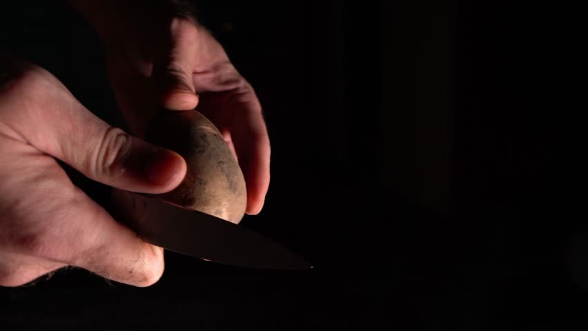 Peeling potatoes with a knife on a black background, cleaning vegetables, preparing food in the kitchen