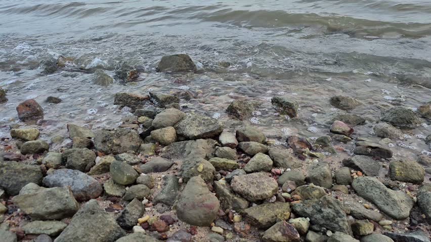 Small ocean waves gently washing over rocks along the shoreline. Close-up coastal scene with natural water movement and rocky beach, ideal for nature, travel, environmental, and relaxation concepts.