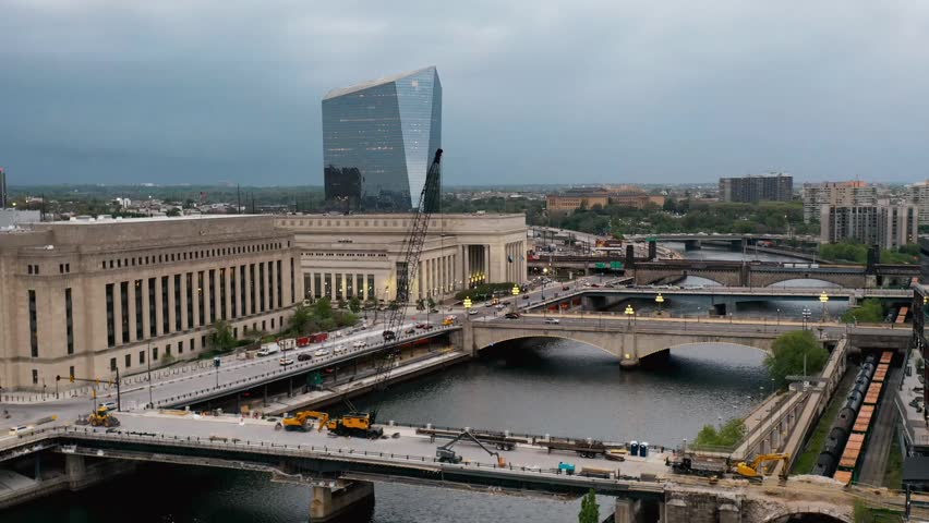 Aerial view of philadelphia showing traffic moving across bridges over the schuylkill river with the historic 30th street station and modern cira centre building dominating the skyline at dusk