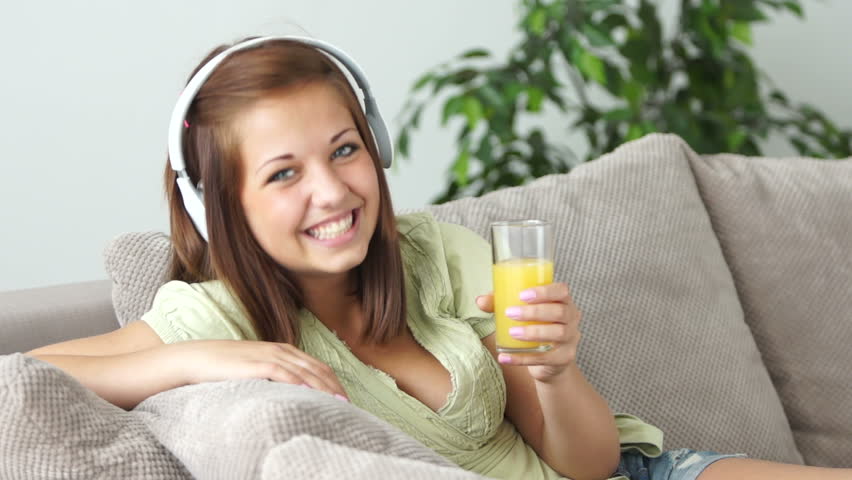Girl listening to music and laughing. She also drinking juice
