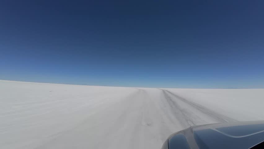 Driving Across Salar De Uyuni Salt Flats In Bolivia Under Clear Blue Sky