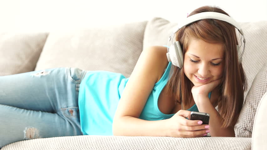 Cute girl lying on couch with phone and listening to music

