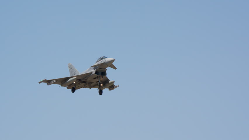 Military fighter jet on final approach with landing gear down in slow motion, warplane descending against blue sky, combat aircraft coming in to land, air force jet