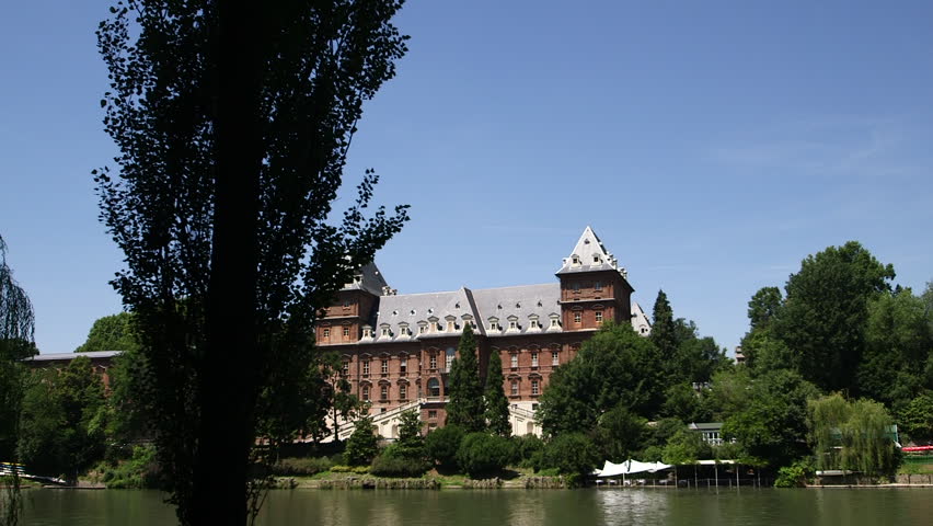 Cinematic slider shot revealing Valentino Castle through trees in Valentino Park, Turin, Italy. Historic riverside landmark surrounded by lush summer greenery.