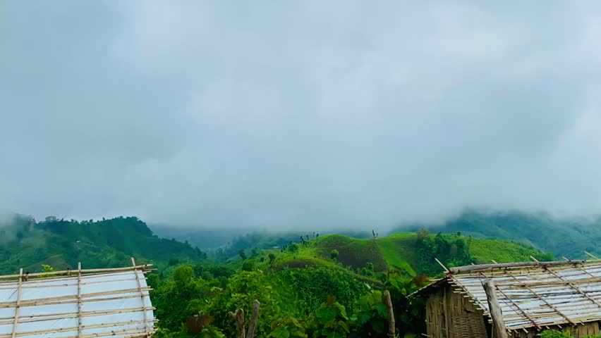 Rolling green hills covered with grass and vegetation under moving fog and clouds in tropical mountain landscape, creating a serene, dramatic countryside view of lush green hills under a partly cloudy sky, sierra, green meadow.