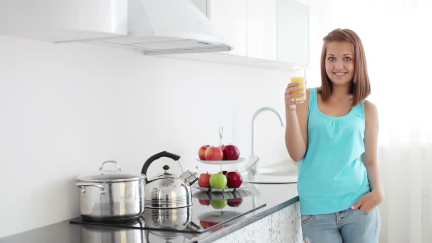 Cute girl standing in kitchen and drinking orange juice
