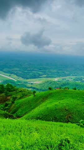 Rolling green hills covered with grass and vegetation under moving fog and clouds in tropical mountain landscape, creating a serene, dramatic countryside view of lush green hills under a partly cloudy sky, sierra, green meadow.