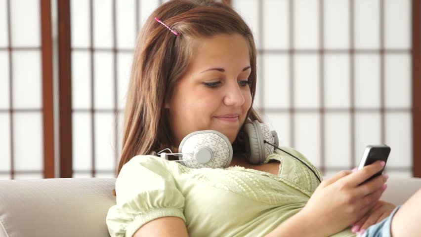 Cute girl sitting on couch with phone and headphones
