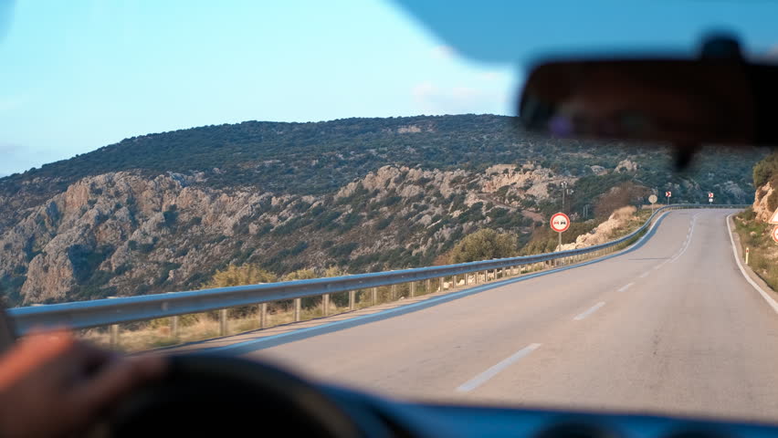 Driver carefully navigating winding mountain road at sunset. Experienced driver navigating challenging mountain roadway during golden evening light, capturing immersive first-person perspective