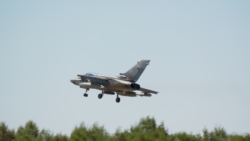 Military fighter jet on approach with gear down flying low over green treetops in slow motion, warplane descending to the runway, combat aircraft coming in to land