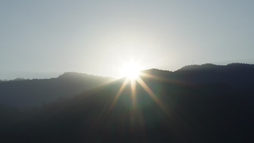 Sunrise over rolling hills with dramatic sun rays illuminating the landscape in a peaceful early morning outdoor scene