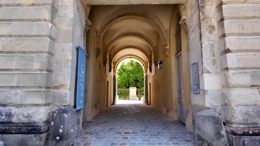 Stone corridor and vaulted archway opening toward the gardens of Fontainebleau Palace in France on a sunny day