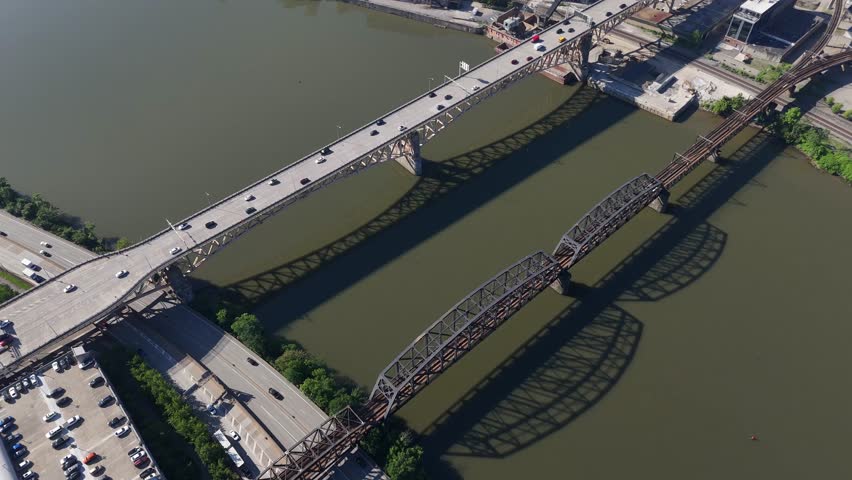 Top-down geometric drone view looking directly down onto historic steel bridge structures spanning across the river in Pittsburgh, PA car driving in rush hours