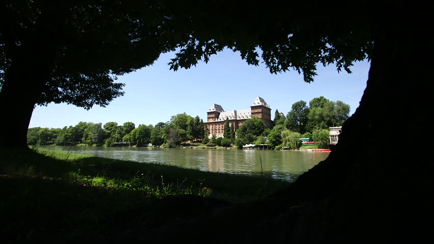 Cinematic slider shot revealing Valentino Castle across the River Po, naturally framed by trees on a sunny day in Turin, Italy