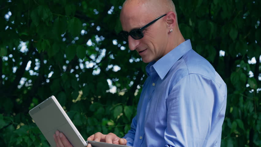 Focused entrepreneur working on a tablet outdoors in a lush, green environment.