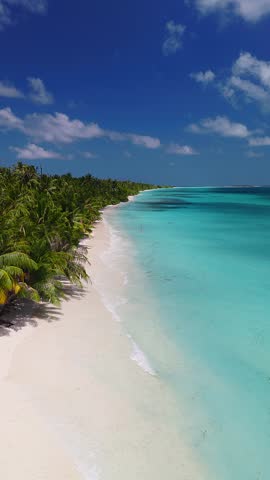 Aerial view of Dhigurah Island, Maldives, with white sand, coconut palms, two cell towers, turquoise lagoon, reef patches, gentle waves, and swimmers with rings.