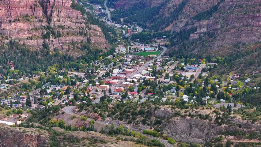 Panoramic aerial view of Ouray, Colorado town known as Switzerland of America in box canyon landscapes with mountainside cliffs and fall foliage tree during autumn season colors in San Juan Mountains - 4K Drone