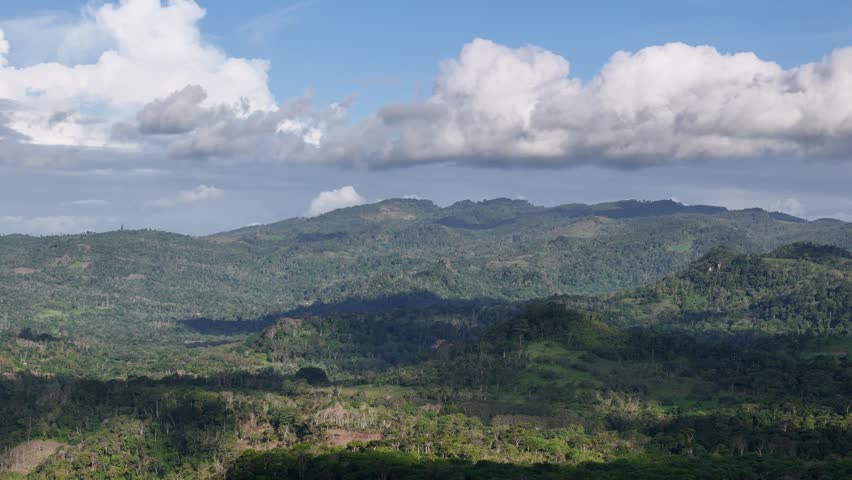 Green hills rise under a blue sky with white clouds. Trees cover the landscape, creating a natural setting.
