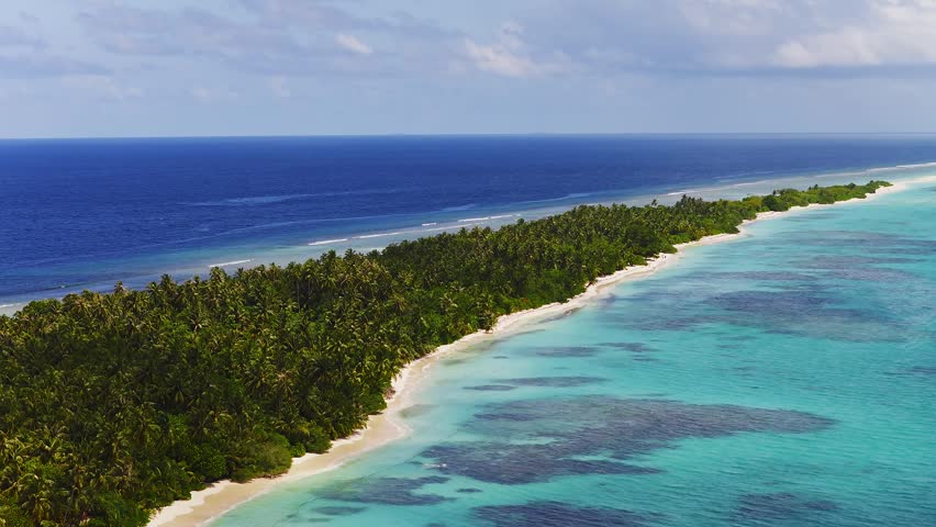 Aerial view of Dhigurah Island, Maldives, long atoll with coconut palms, white sand, turquoise lagoon, coral reefs, gentle waves, small boats, bright daytime light