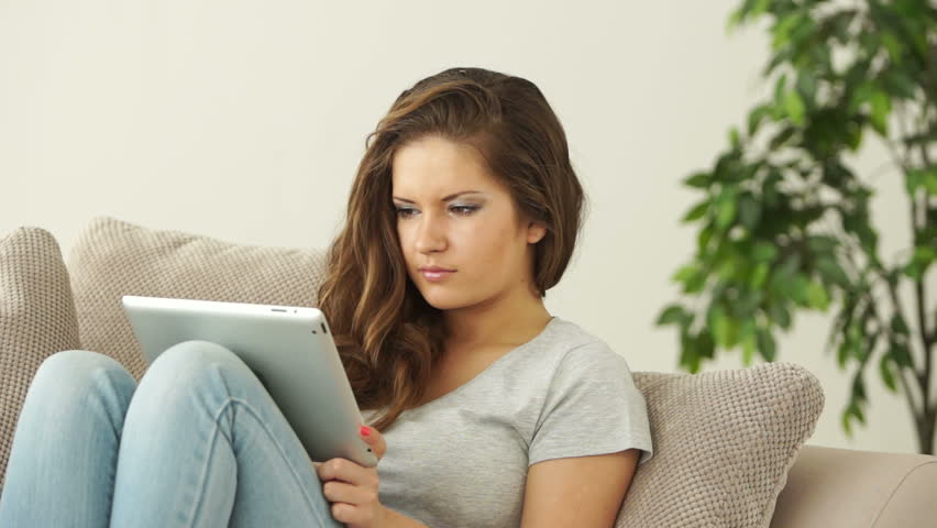 Young adult sitting on sofa with tablet and thinking about something
